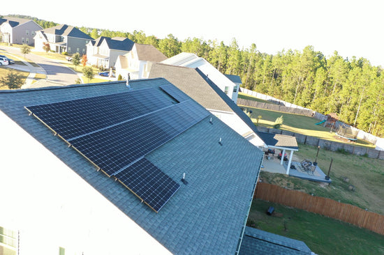 Wide drone view of a home with a solar array installed across the rear roof plane.